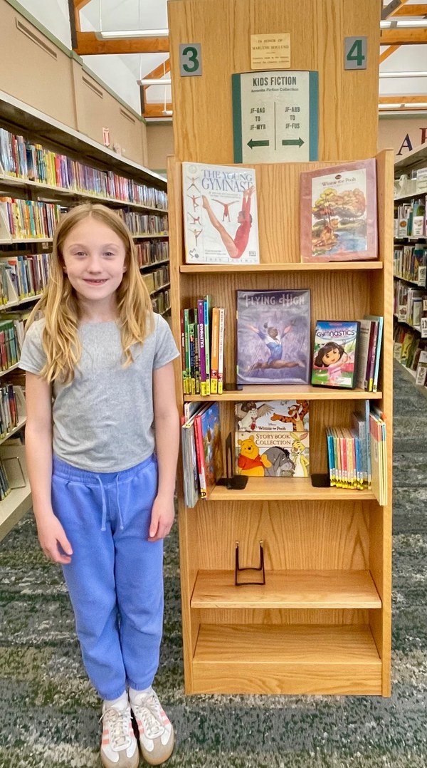 Melany in front of her bookshelf display.